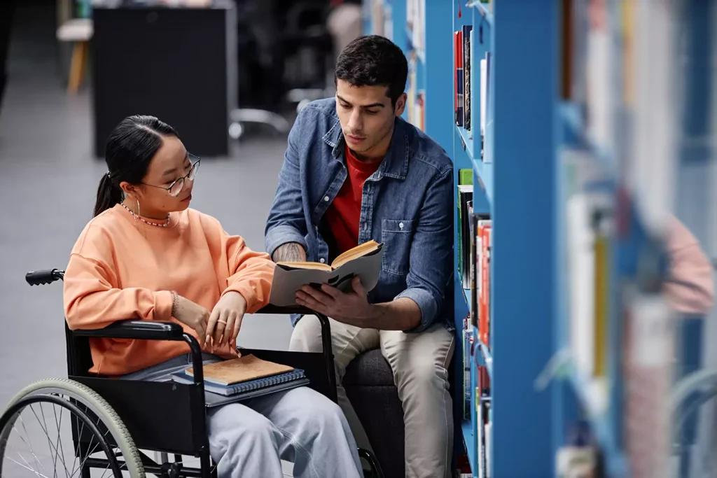 Disabled woman in wheelchair reading book at library with friend