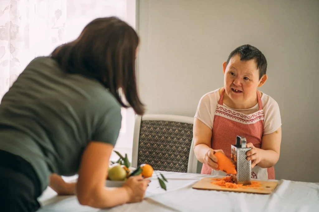 Disabled woman with support worker at home grating a sweet potato
